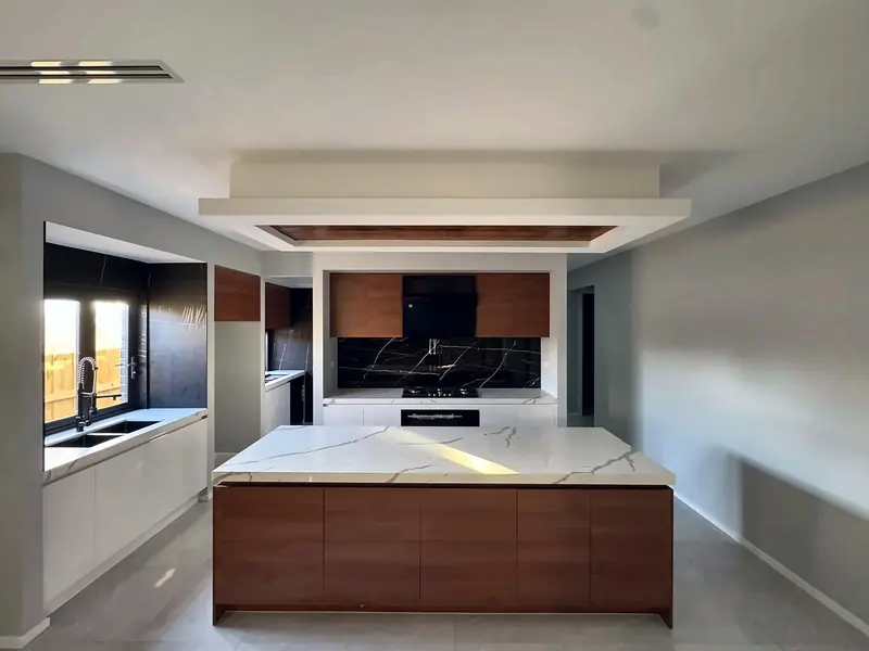 Wide view of a walnut-look island kitchen with white base cabinets and a black splashback, by Maya Cabinets in Melbourne